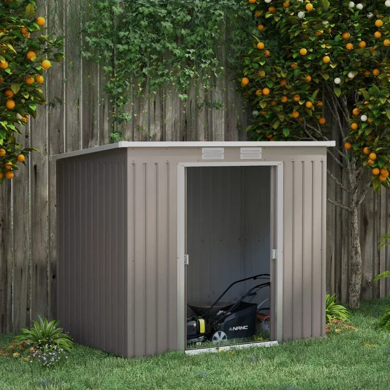 Light grey metal shed on a lawn in front of a fruit tree and fence, with a lawnmower stored inside