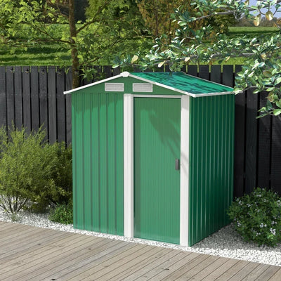 Green metal garden shed standing on decking in front of a dark painted fence and shrubs