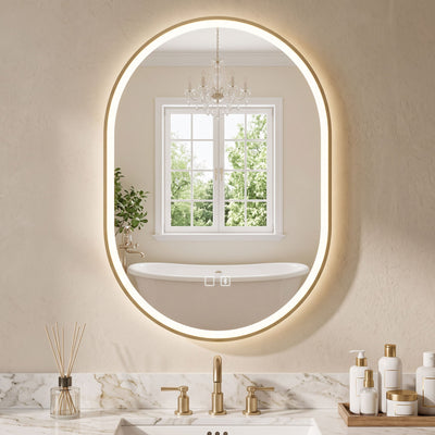 Gold oval LED mirror lit above a vanity with a window and bath reflected in it