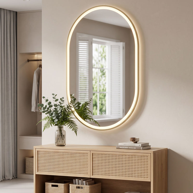 Gold oval LED mirror mounted vertically above a wooden sideboard with a plant