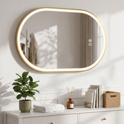 Gold oval LED mirror mounted horizontally above a white chest of drawers