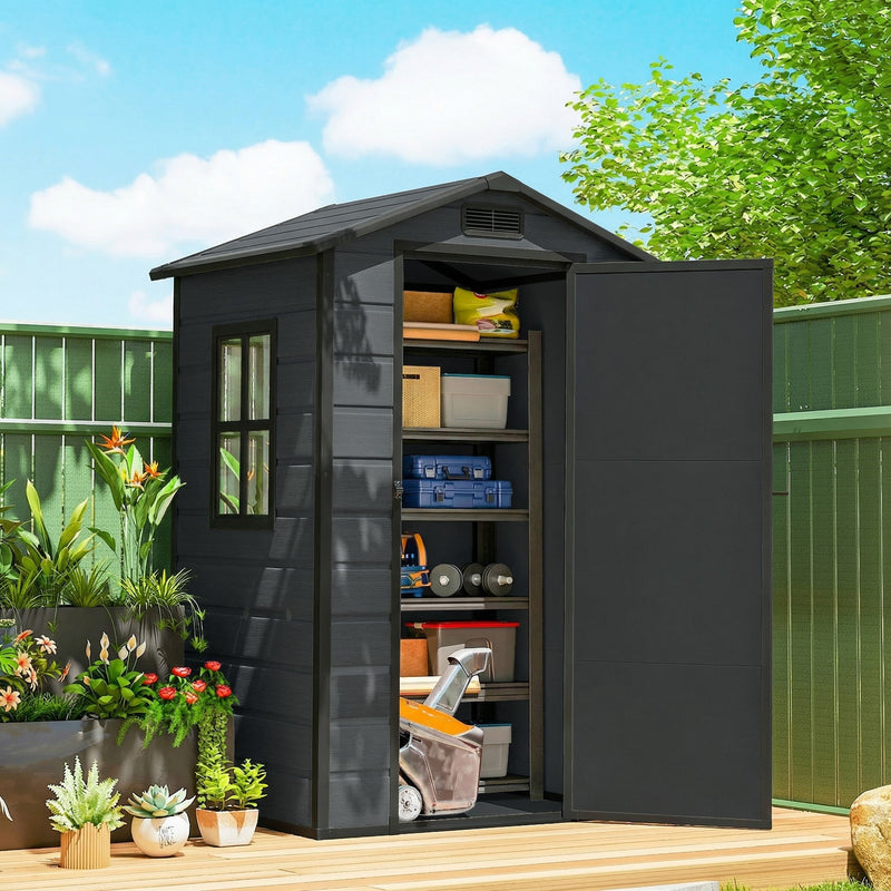 Dark grey resin garden shed on a patio beside pot plants under a blue sky