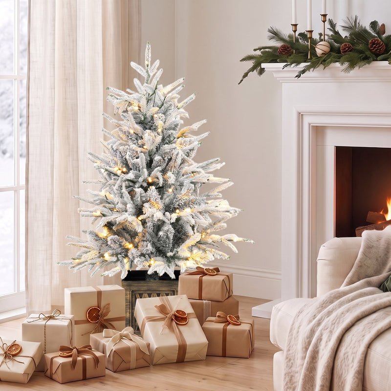 Flocked table tree with warm white lights beside a fireplace and wrapped gifts