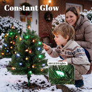 Child pointing at a colourful LED Christmas tree in the snow with 60 LED lights close-up