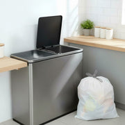 Tied white drawstring bin bag standing next to a stainless steel double kitchen bin