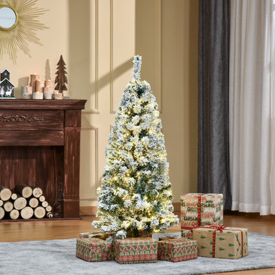 4ft snow flocked Christmas tree lit up in a living room beside a fireplace with wrapped gifts