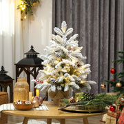 Lit flocked mini tree with berries on a table beside a lantern and grey curtains