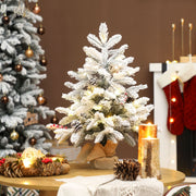 Lit flocked mini tree on a round table beside red stockings and a fireplace