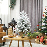 Flocked mini tree on a wooden table in a living room with a decorated tree behind