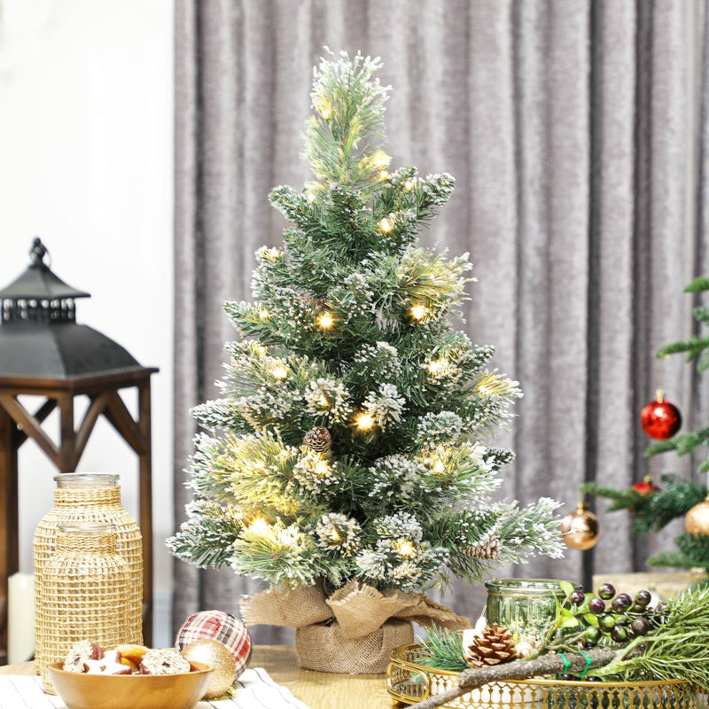Lit mini flocked tree on a side table beside a lantern and grey curtains