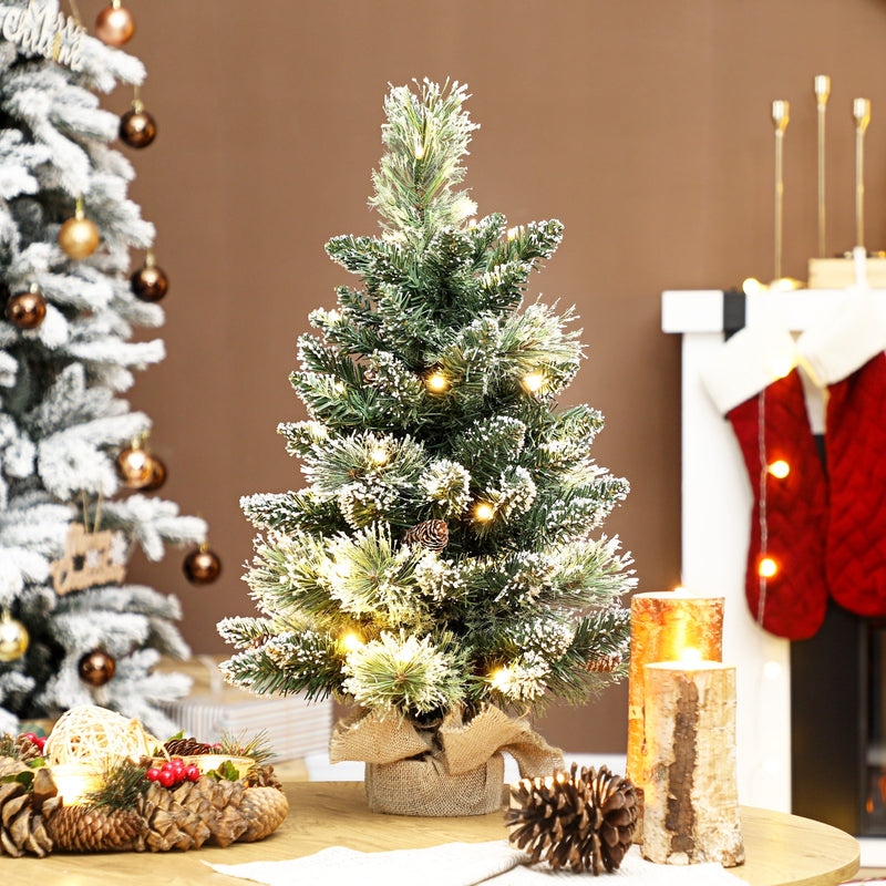 Lit mini flocked Christmas tree on a table beside red stockings and a fireplace