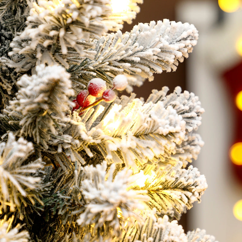 Close-up of snow-flocked branch tips with red berries and warm white lights