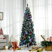 Slim pre-lit Christmas tree with white-tipped branches in a living room beside an armchair and cushions