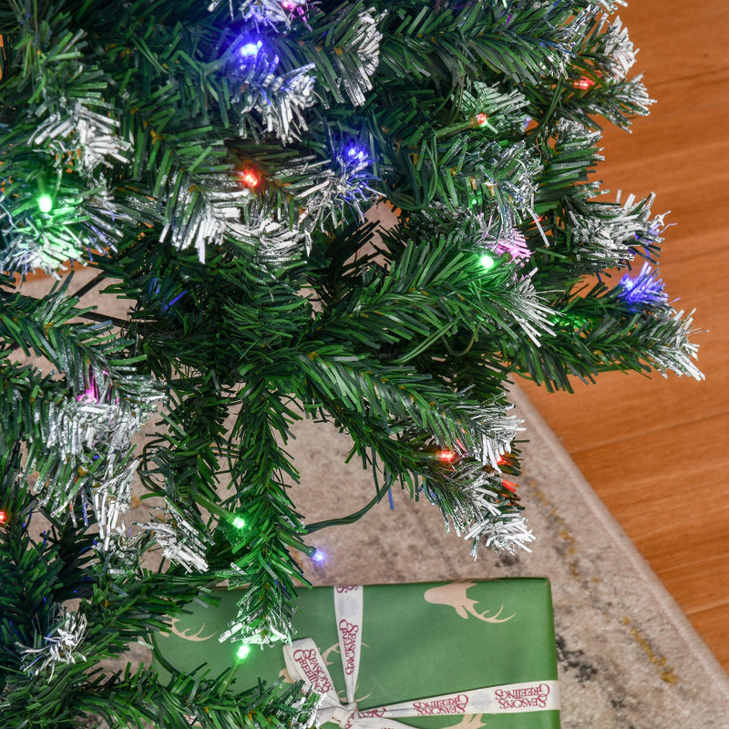 Close-up of green branches with white tips and LED lights beside a wrapped present