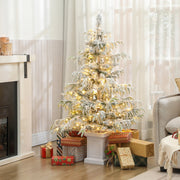 4ft flocked Christmas tree glowing with warm white lights next to a grey armchair