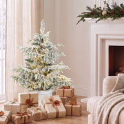 3ft snow flocked Christmas tree beside a fireplace with wrapped gifts around the pot