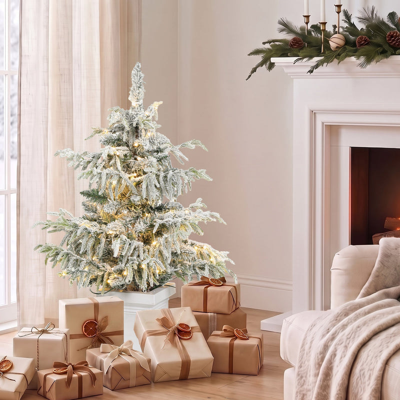 3ft snow flocked Christmas tree beside a fireplace with wrapped gifts around the pot