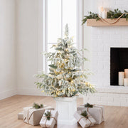 3ft flocked Christmas tree in a white pot beside a white brick fireplace with gifts