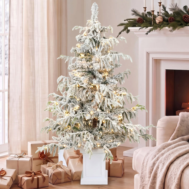 4ft snow flocked Christmas tree beside a fireplace with wrapped gifts around the pot