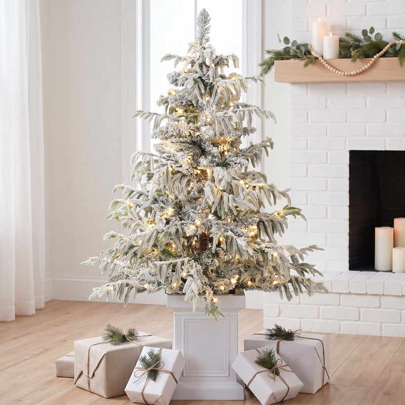 4ft flocked Christmas tree in a white pot beside a white brick fireplace with gifts