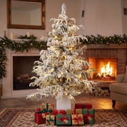 4ft flocked Christmas tree in front of a lit fireplace with red and green gifts on a rug