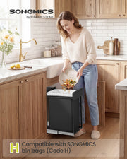 Woman scraping vegetable peelings into the open pull-out kitchen bin under a sink
