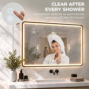 Woman in a towel wrap in front of the black LED mirror with a clear demisted centre after a shower