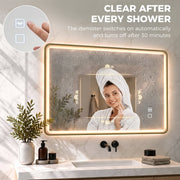 Woman in a towel wrap in front of the gold LED mirror with a clear demisted centre after a shower