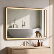 Gold LED bathroom mirror mounted horizontally above a wooden vanity with a bath in the reflection