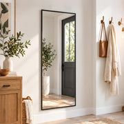 Full length mirror leaning in a hallway beside a front door and coat hooks