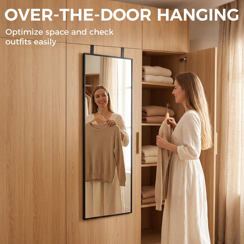 Woman holding a top while checking her outfit in the over-door mirror beside a wardrobe