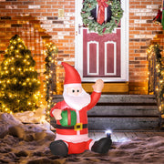 Sitting inflatable Santa beside a front door with a wreath, a lit tree and snow