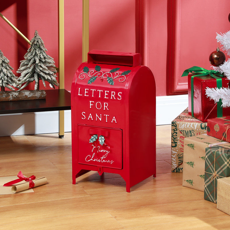 Red Santa postbox standing on a wooden floor beside a Christmas tree and presents