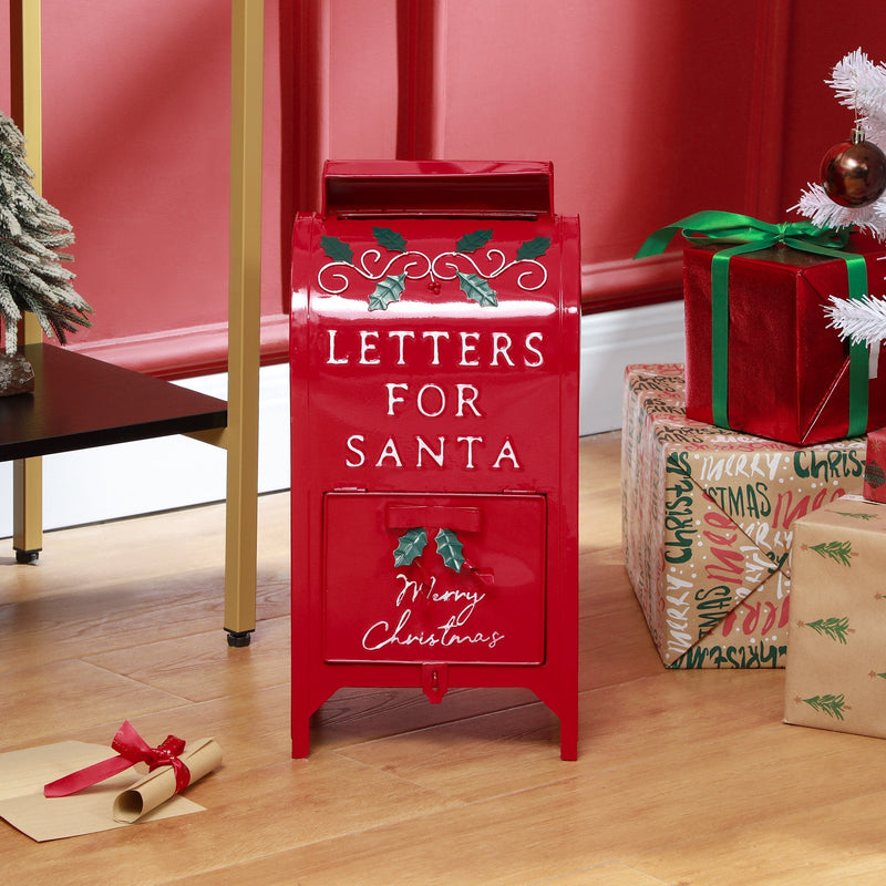 Red Christmas postbox on the floor beside wrapped gift boxes and a ribbon-tied letter