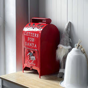 Red Santa postbox standing on a shelf beside a gnome and a white bell ornament