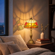 Lit tulip lamp on a bedside table next to cushions and books at dusk
