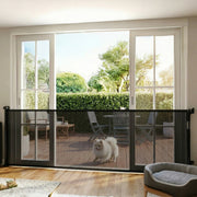 Black retractable dog gate across patio doors with a fluffy dog on the decking