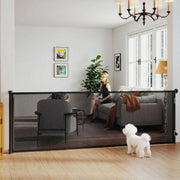 Black retractable dog gate across a living room with a small white dog in front