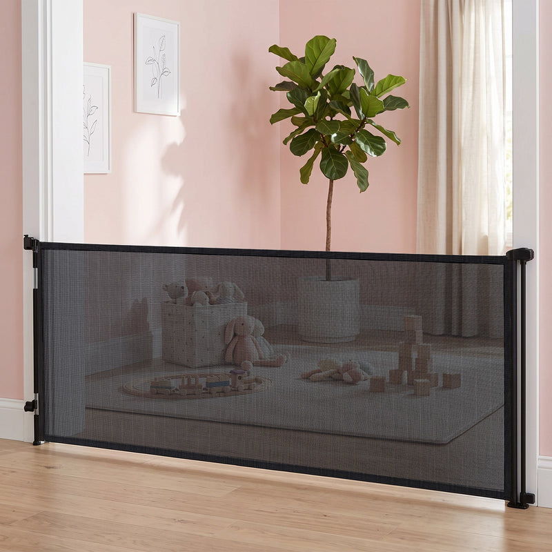 Black mesh dog gate closed across a pink playroom with toys behind it