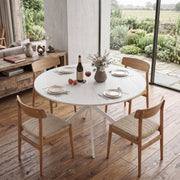Round table set for dinner with wooden chairs beside a garden window