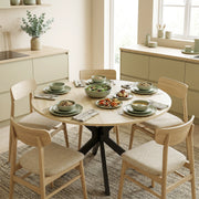 Round table laid with green dishes and surrounded by four wooden chairs on a rug