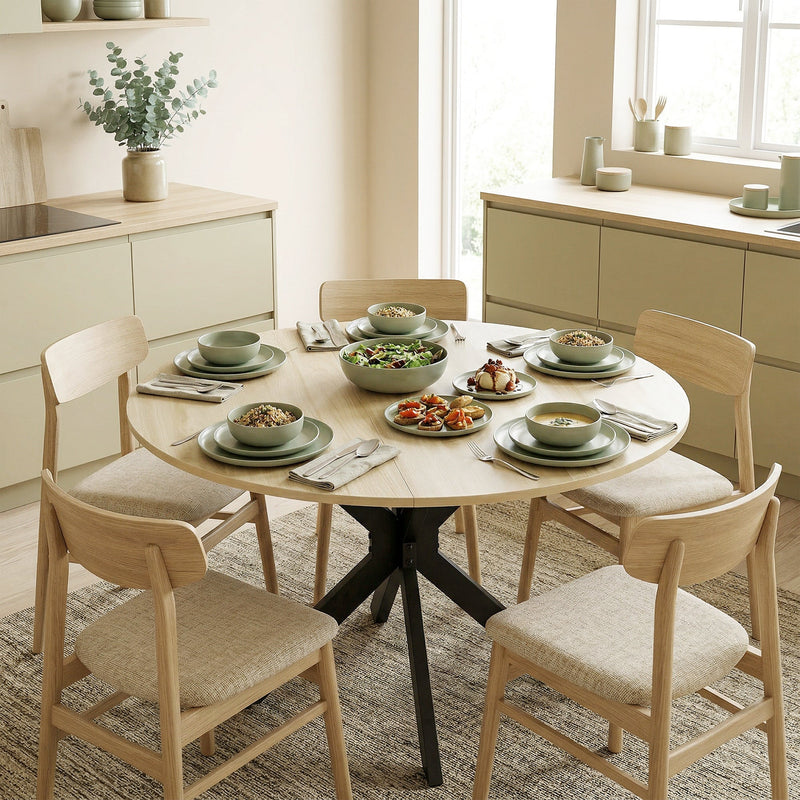 Round table laid with green dishes and surrounded by four wooden chairs on a rug