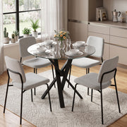 Round glass dining table set for four with grey chairs in a bright kitchen