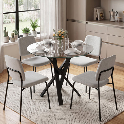 Round glass dining table set for four with grey chairs in a bright kitchen