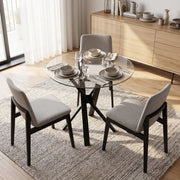 Round glass dining table with light grey chairs beside a wooden sideboard
