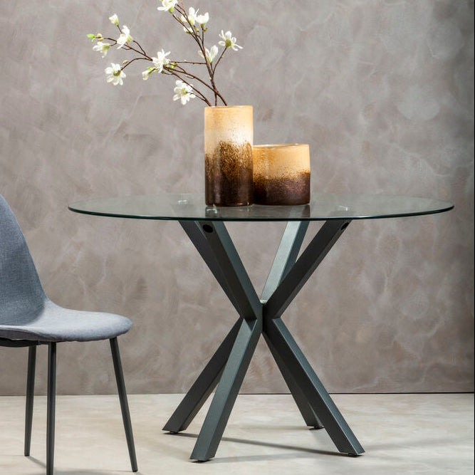 Round glass dining table with grey metal legs in a lifestyle dining setting