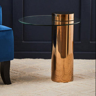 Round clear glass side table with rose gold pedestal styled beside a sofa