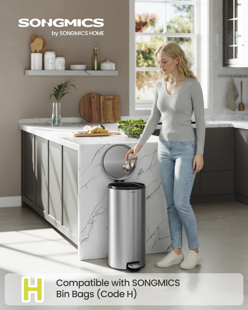 Woman dropping food scraps into the silver pedal bin beside a marble kitchen island