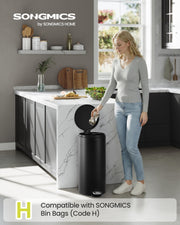 Woman dropping food scraps into the black pedal bin beside a marble kitchen island
