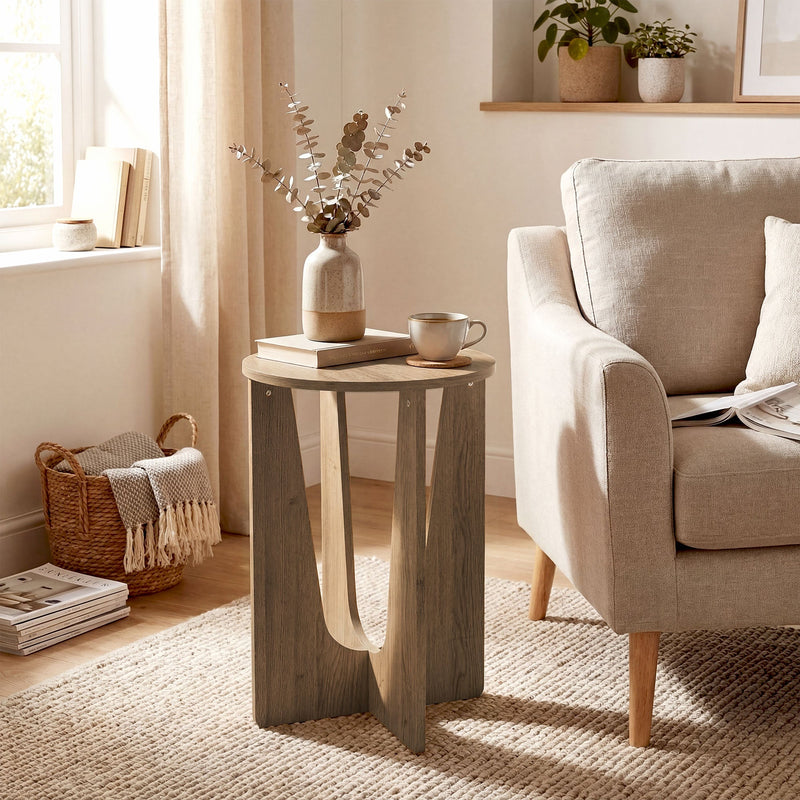 Round side table beside a linen armchair holding a vase, books and a mug